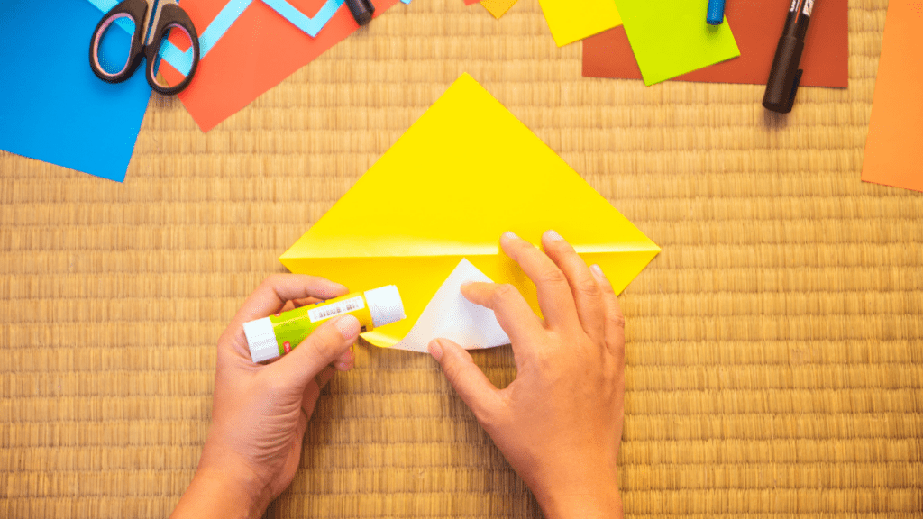 A person making a paper kite with scissors and glue