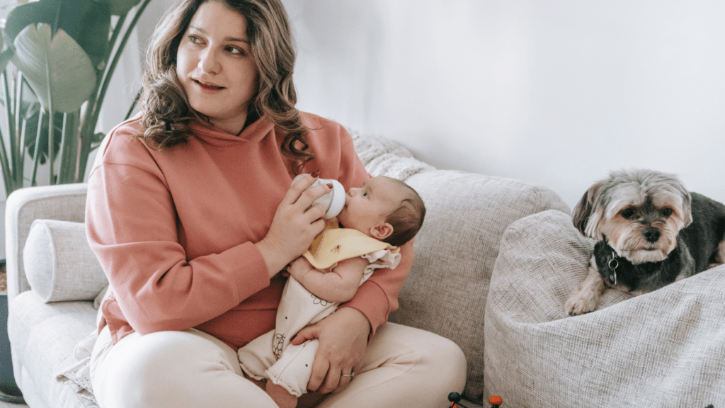 A person sitting on a couch with a baby and a dog
