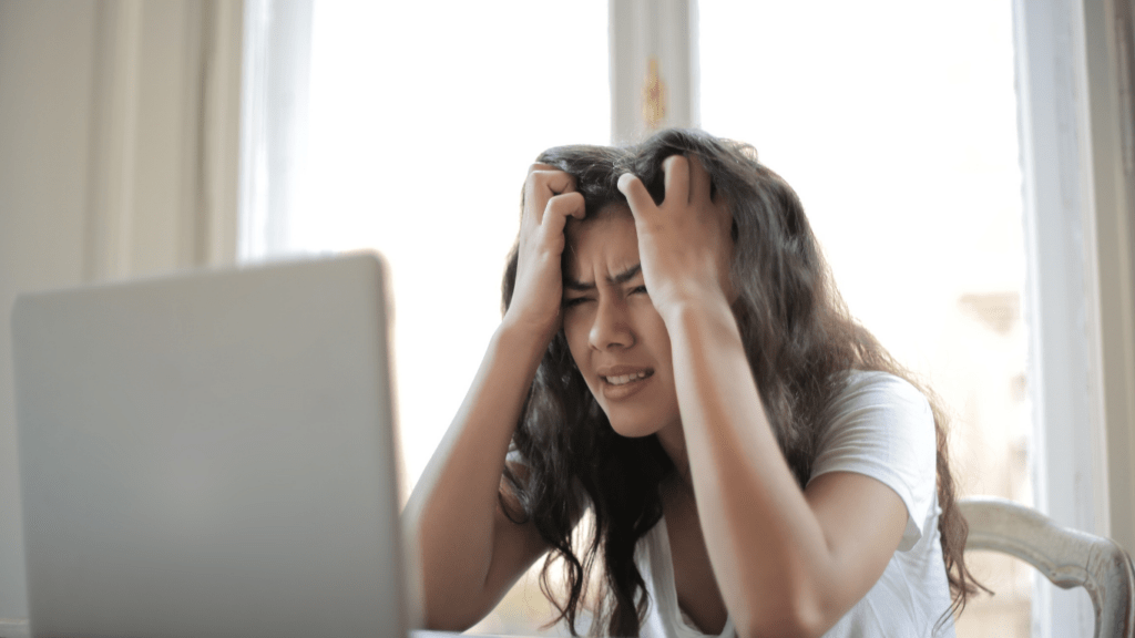 a person sitting in front of a laptop with their hands on their head