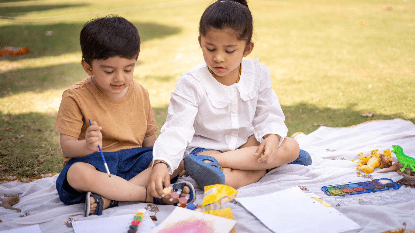 two children are sitting on the grass and painting