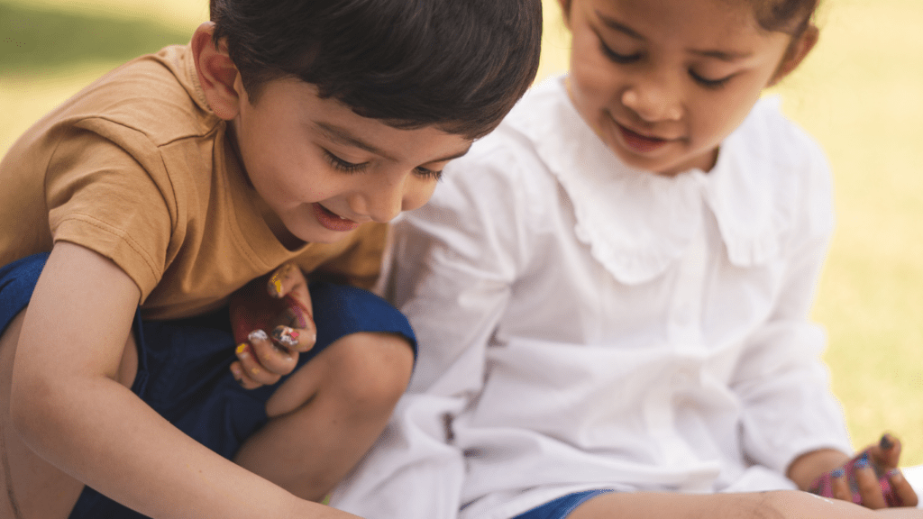two children are sitting on the grass and painting