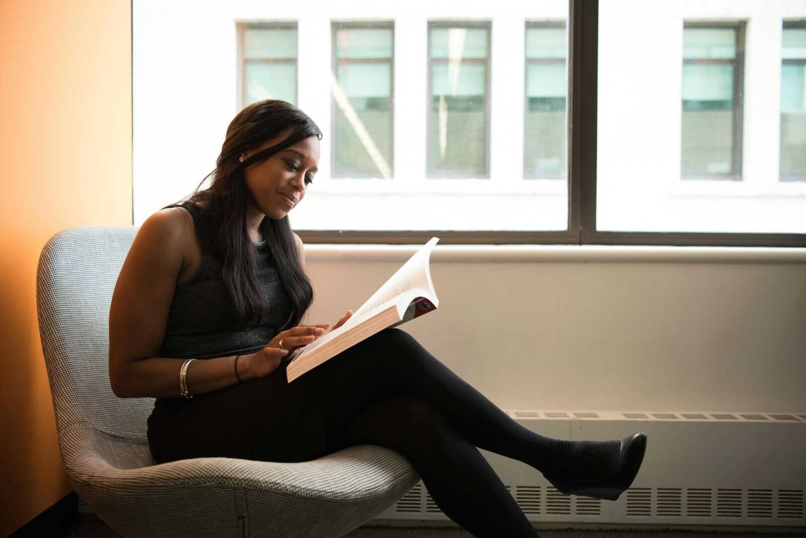 A thoughtful woman reading a book while sitting by a window indoors.