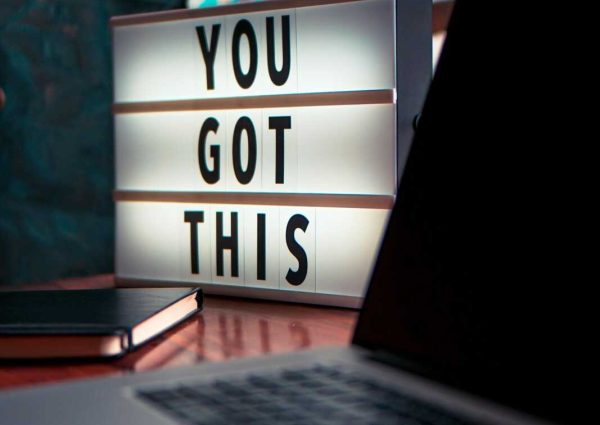 pexels-photo-2740954-2740954 Illuminated lightbox with a motivational quote beside a laptop, promoting productivity.